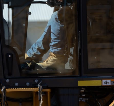 Operator inside a John Deere motor grader cab working at a construction site.