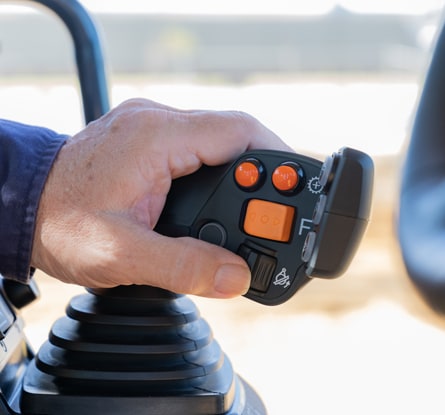 Hand operating a machine control joystick inside a construction vehicle cab.