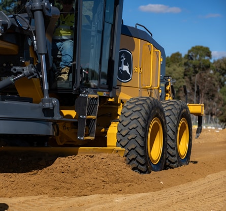 John Deere motor grader moves soil while grading a dirt road at a construction site.