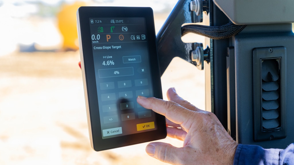Operator uses a touchscreen display to adjust grading settings inside a John Deere motor grader.