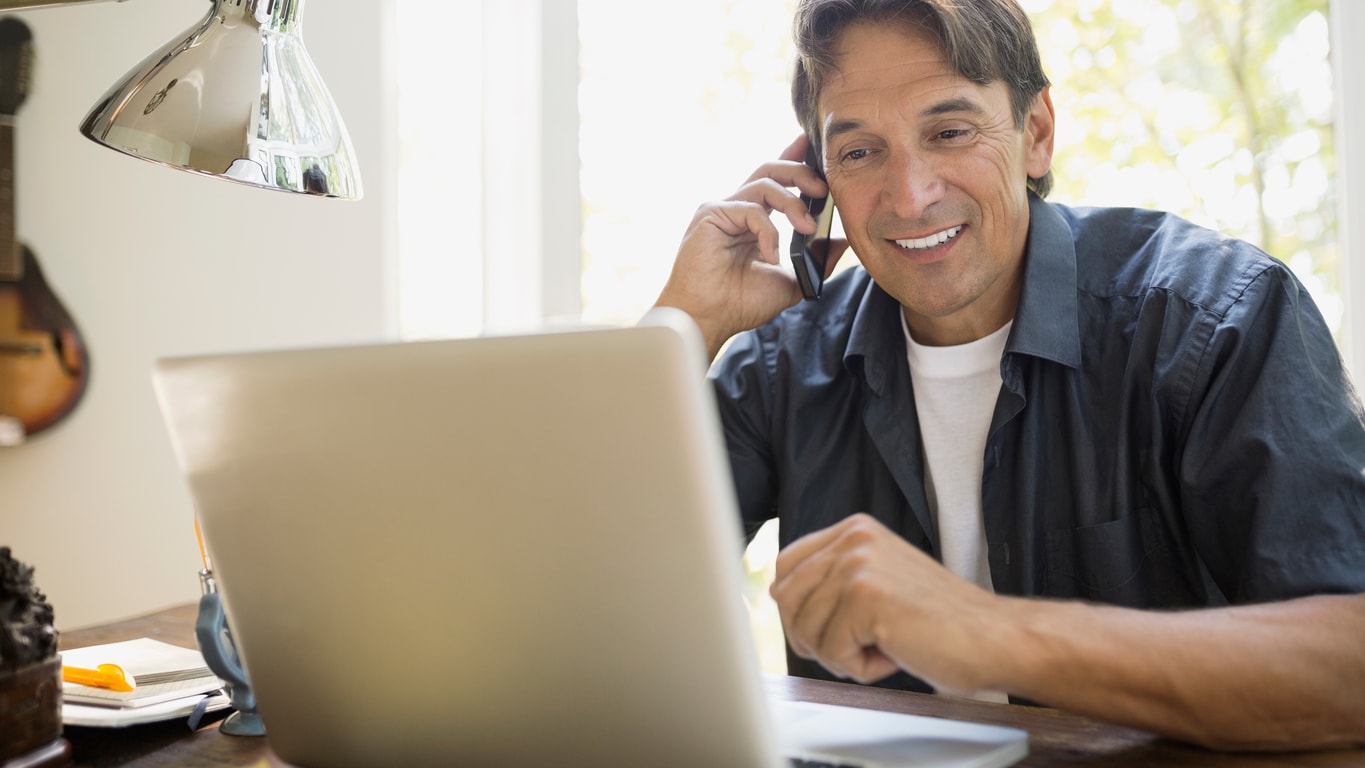 Man using a phone and looking at a laptop computer