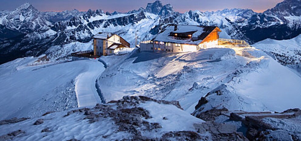 Cabins on a high mountain peak with bright lights turned on.