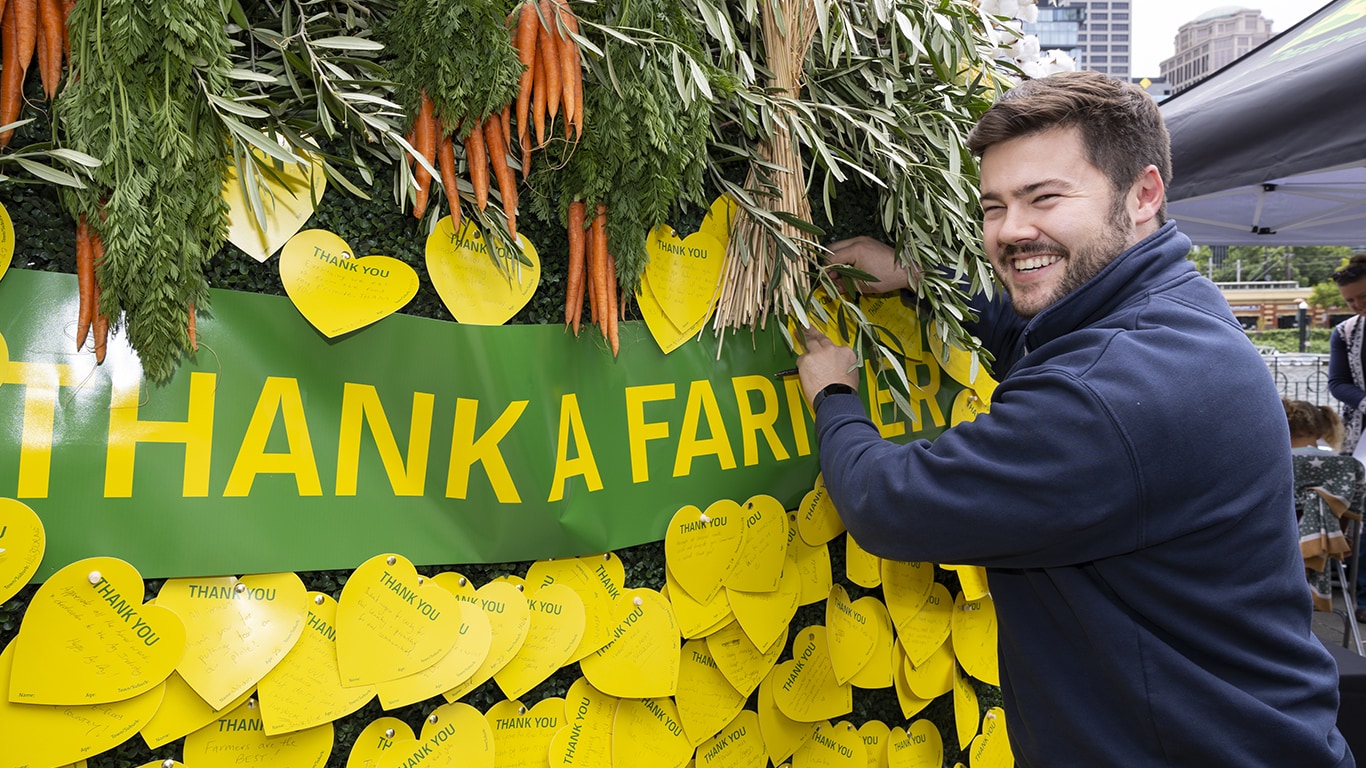A man smiling at the camera as he pins a thank you message to the Thank a Farmer wall.