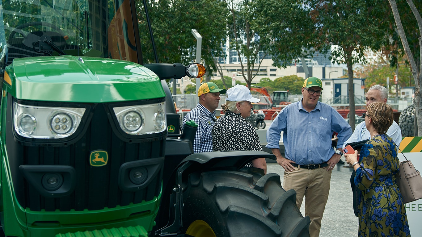 A group of people standing next to a John&nbsp;Deere tractor.