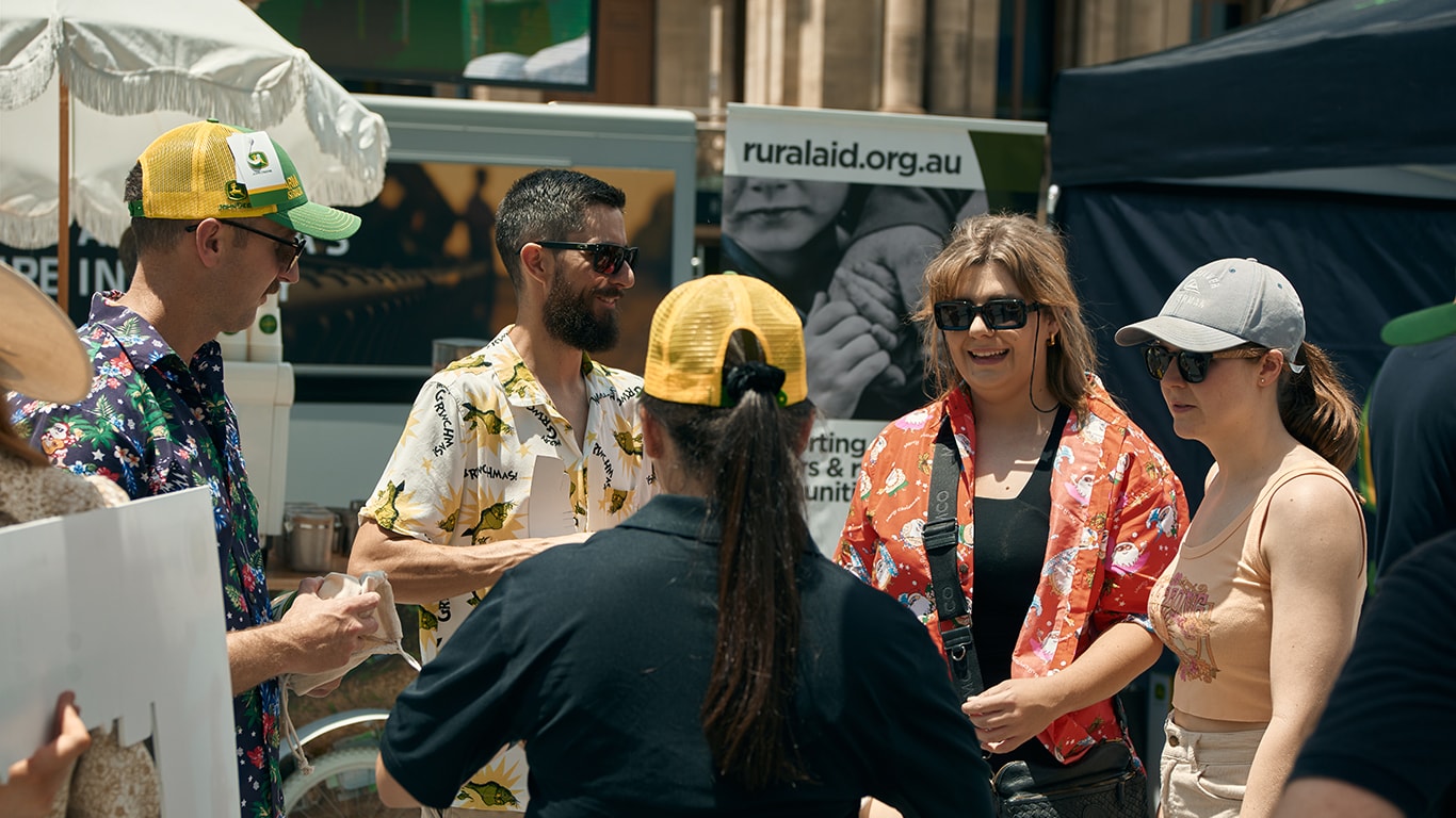 A group of people standing outside near a RuralAid banner.