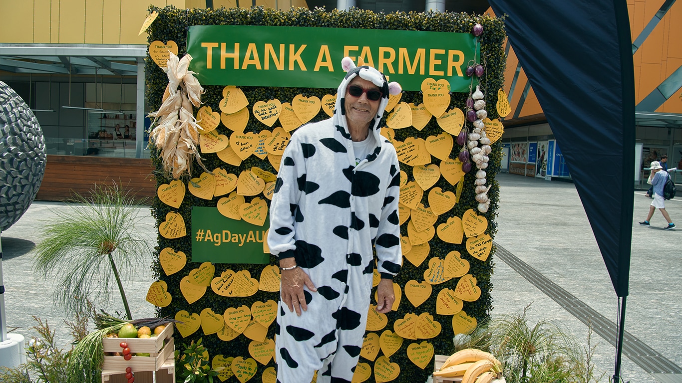 A man in a cow onesie standing in front of the Thank a Farmer wall.
