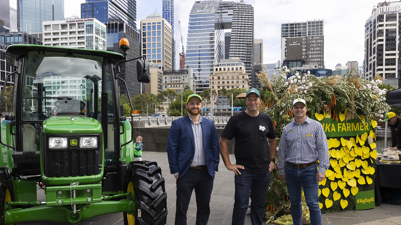 A group of men standing between a John&nbsp;Deere tractor and the Thank a Farmer wall.