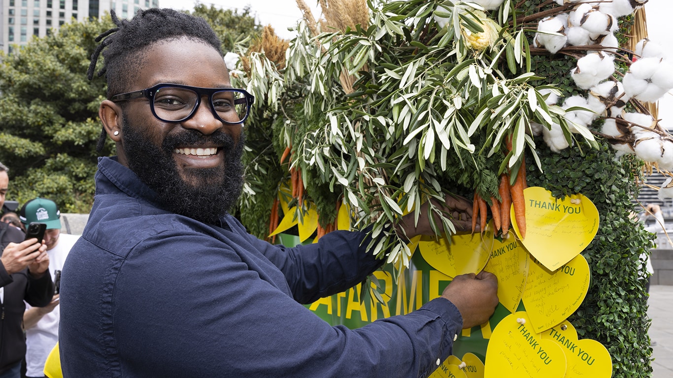 A man smiling at the camera as he pins a thank you message to the Thank a Farmer wall.