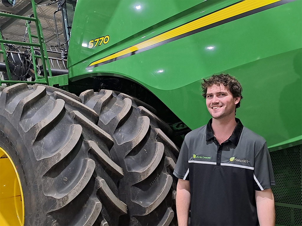 young brown haired man standing in front of large tractor tire