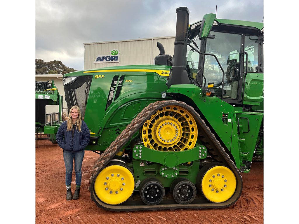 young blonde woman standing in front of John Deere tractor
