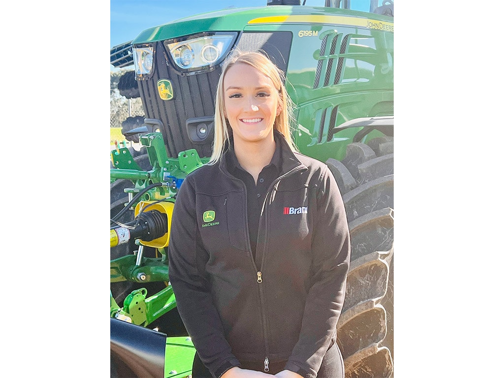 young blonde woman standing in front of John Deere tractor