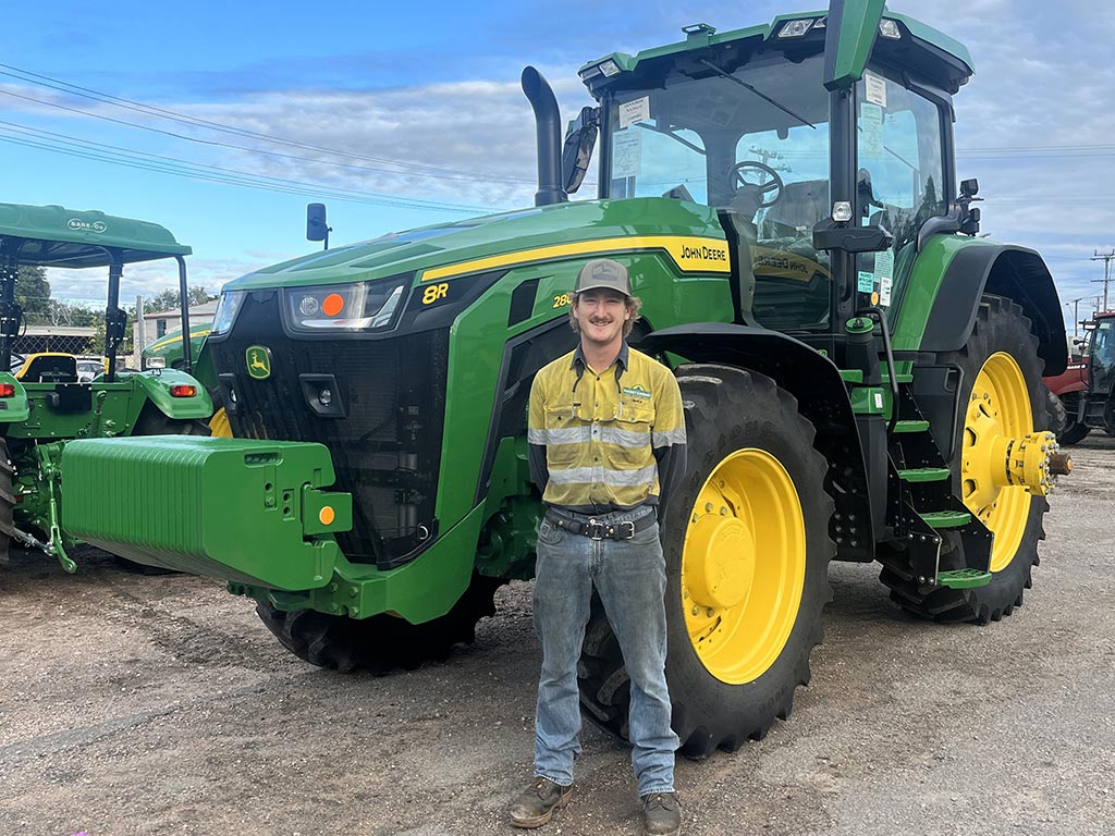 young man standing in front of John Deere tractor