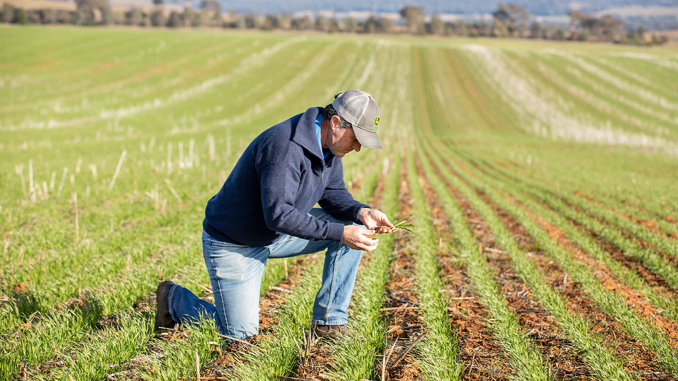 man in John&nbsp;Deere cap kneeling down in broadacre field