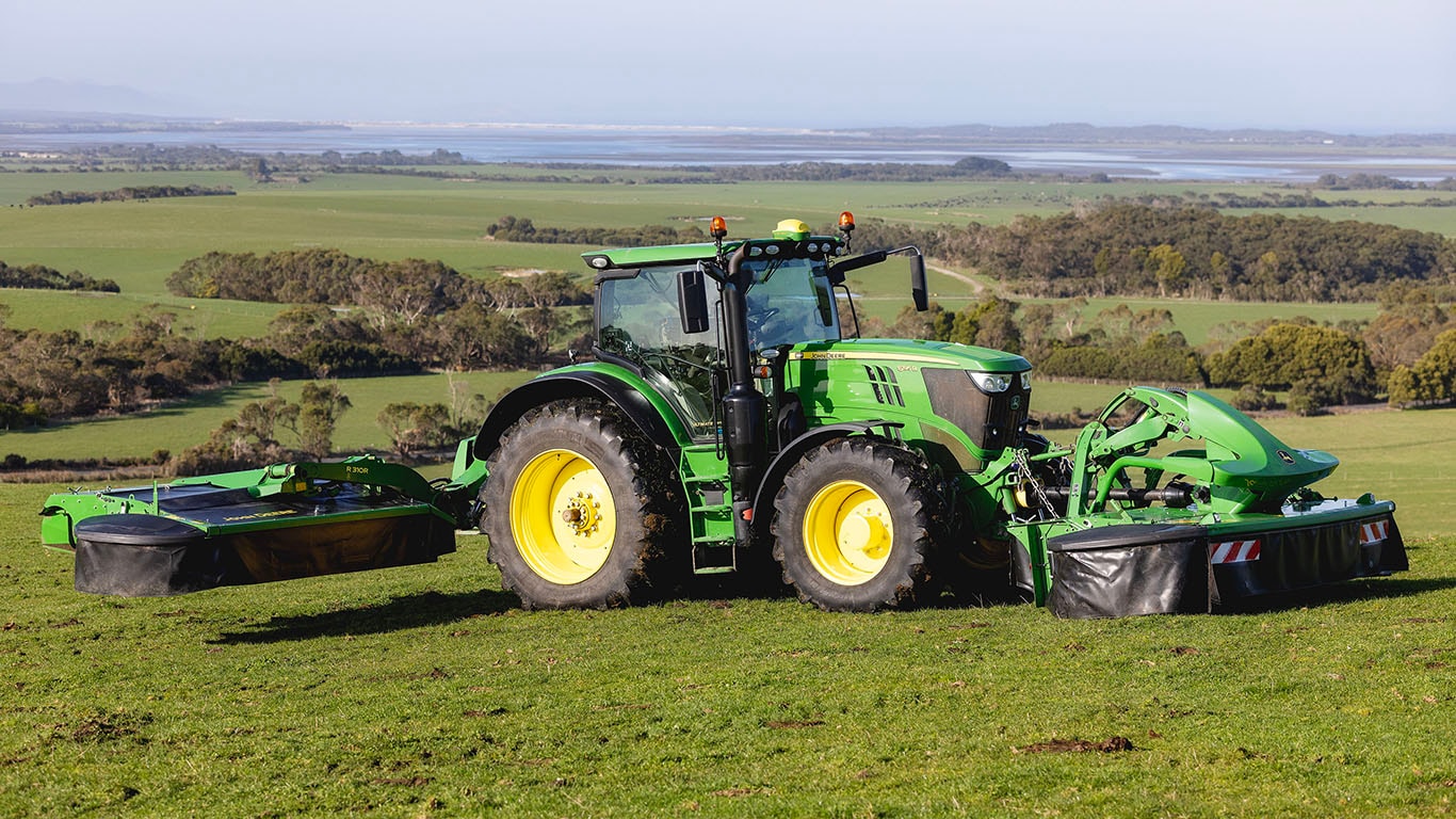 R310R Mower Conditioner pulled by a Deere tractor over rolling hills