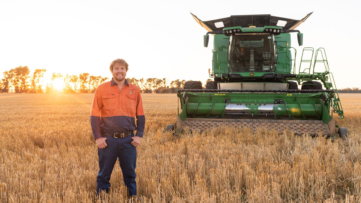 Broden Holland standing in a paddock with the X9 Combine Harvester