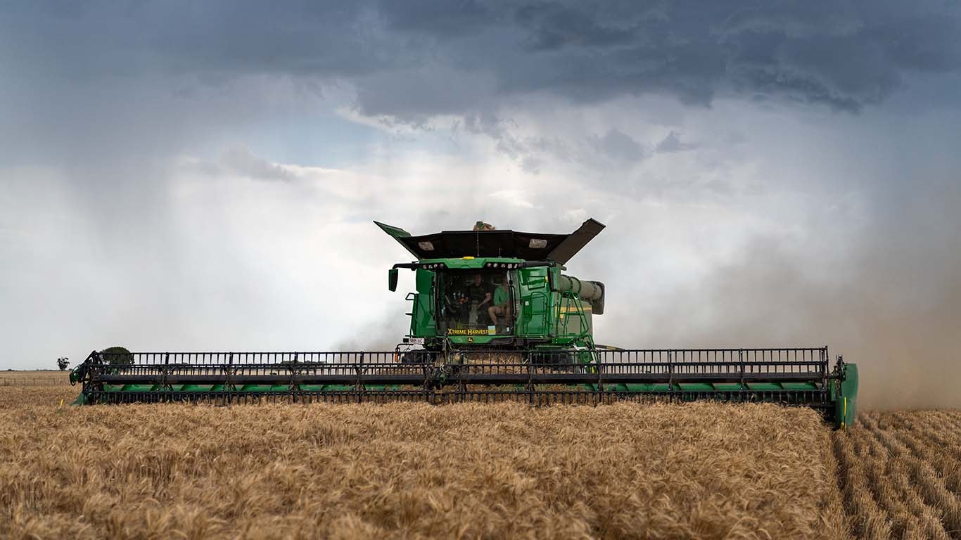 John Deere X9 Combine Harvester in a wheat field with stormy sky.