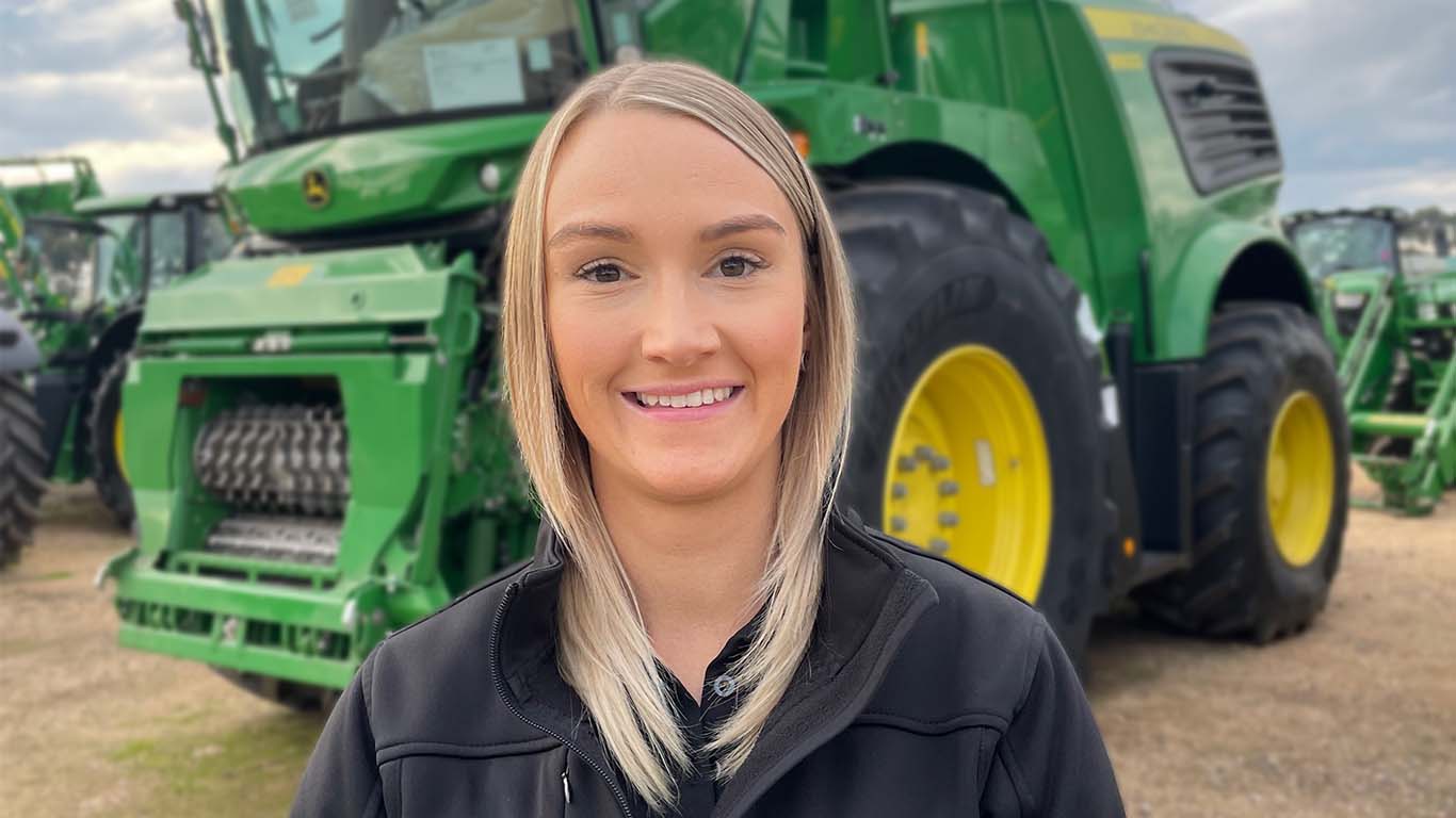 Sarah Lewis standing in front of John Deere machinery.