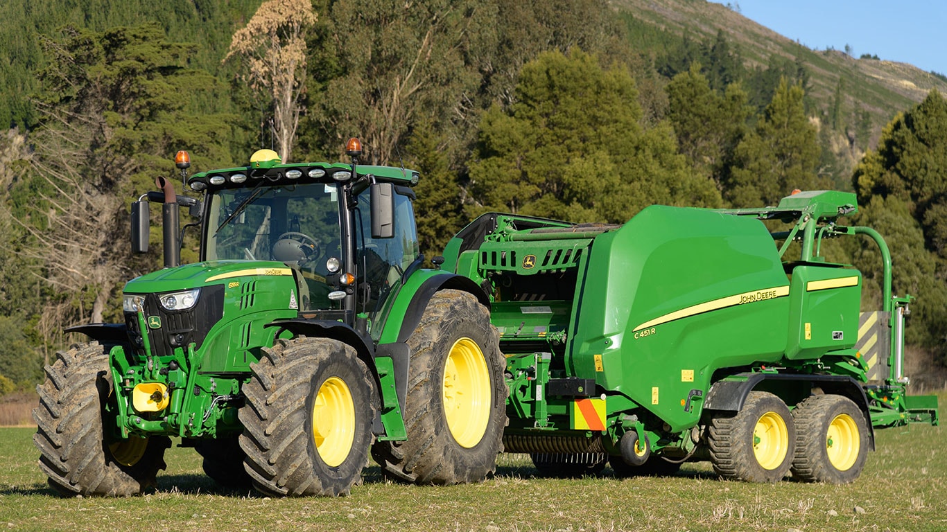 John Deere machinery in a field with a hill behind