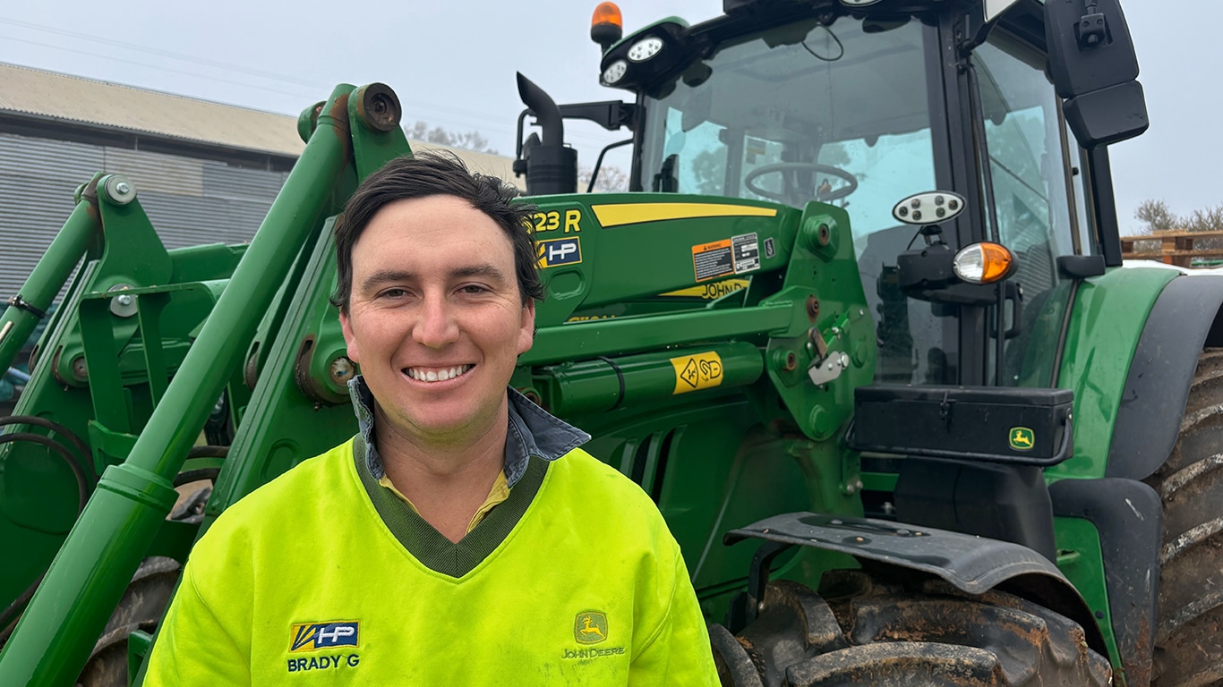 Brady Gunter smiling in front of a tractor with a 623R attachment
