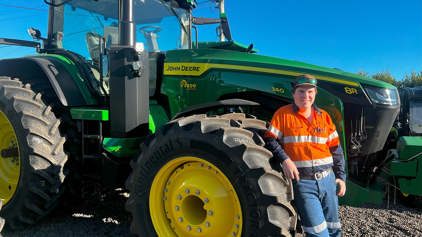 Zac Weir smiling in front of a 8R 340 tractor