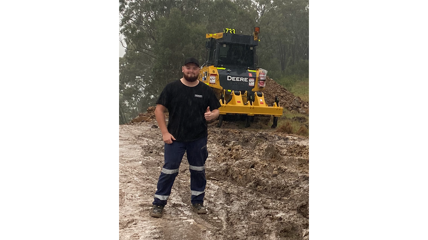 Hayden Cox smiling with a thumbs up in front of construction equipment
