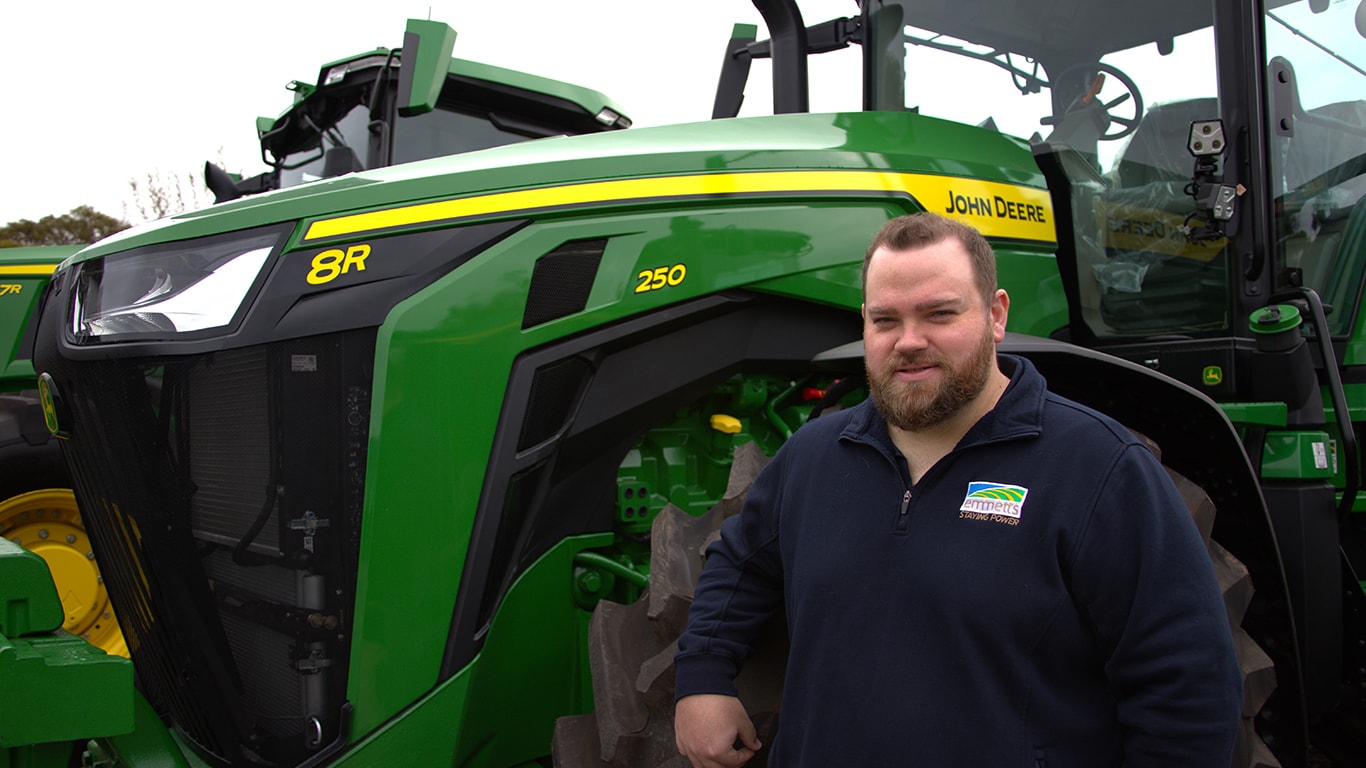 Alex Tyler smiling in front of a 8R 250 tractor