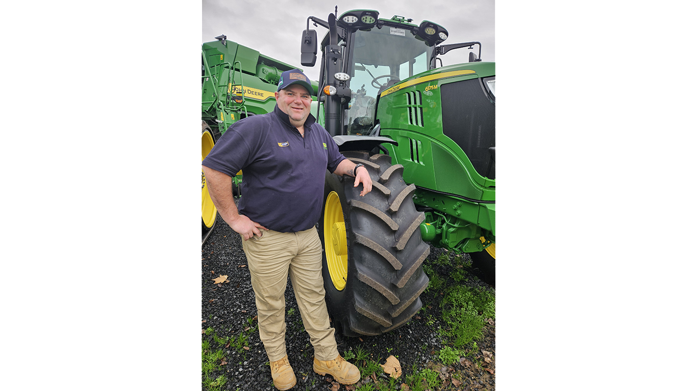 Andrew Keller smiling leaning on a 6175M tractor