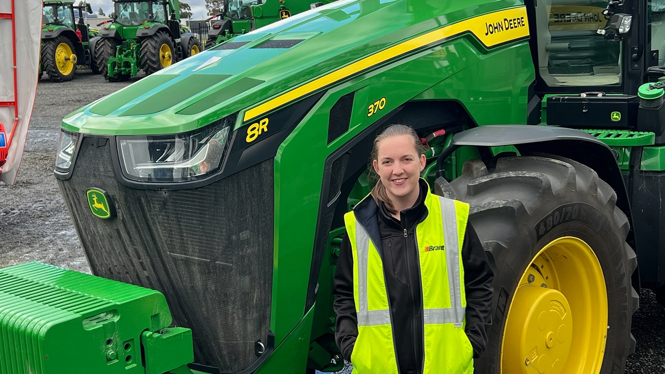Kirsten Rush smiling in front of a 8R 370 tractor