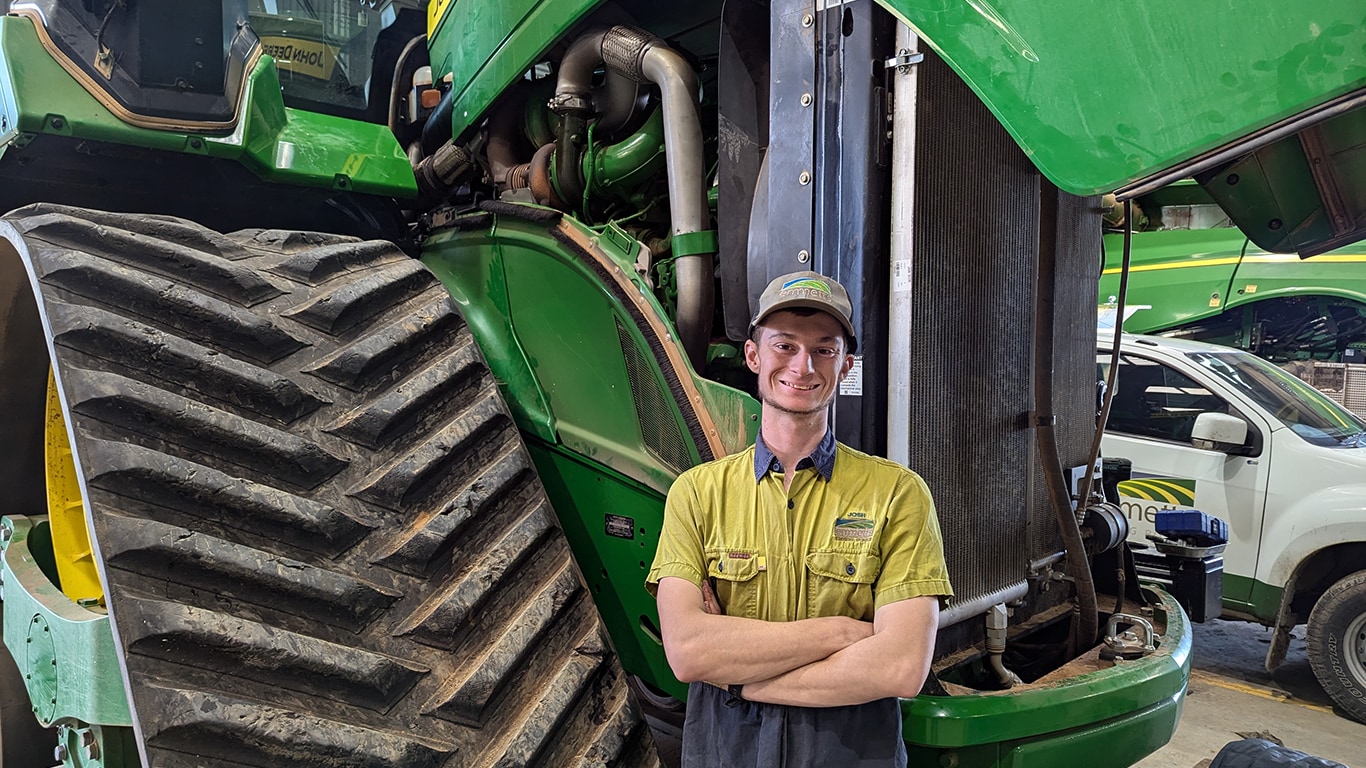 Josh Kramer smilng with arms crossed in front of a tracked tractor with its hood up
