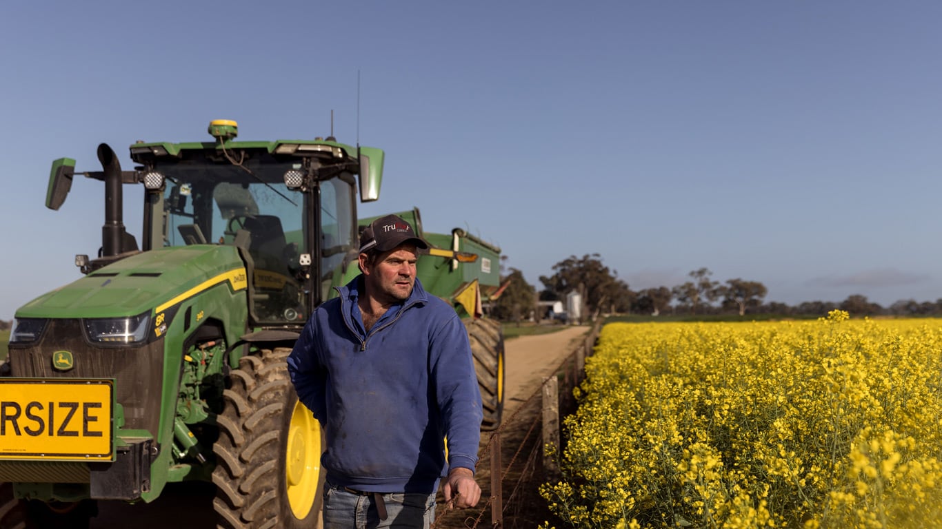 Farmer standing beside wool field in front of tractor