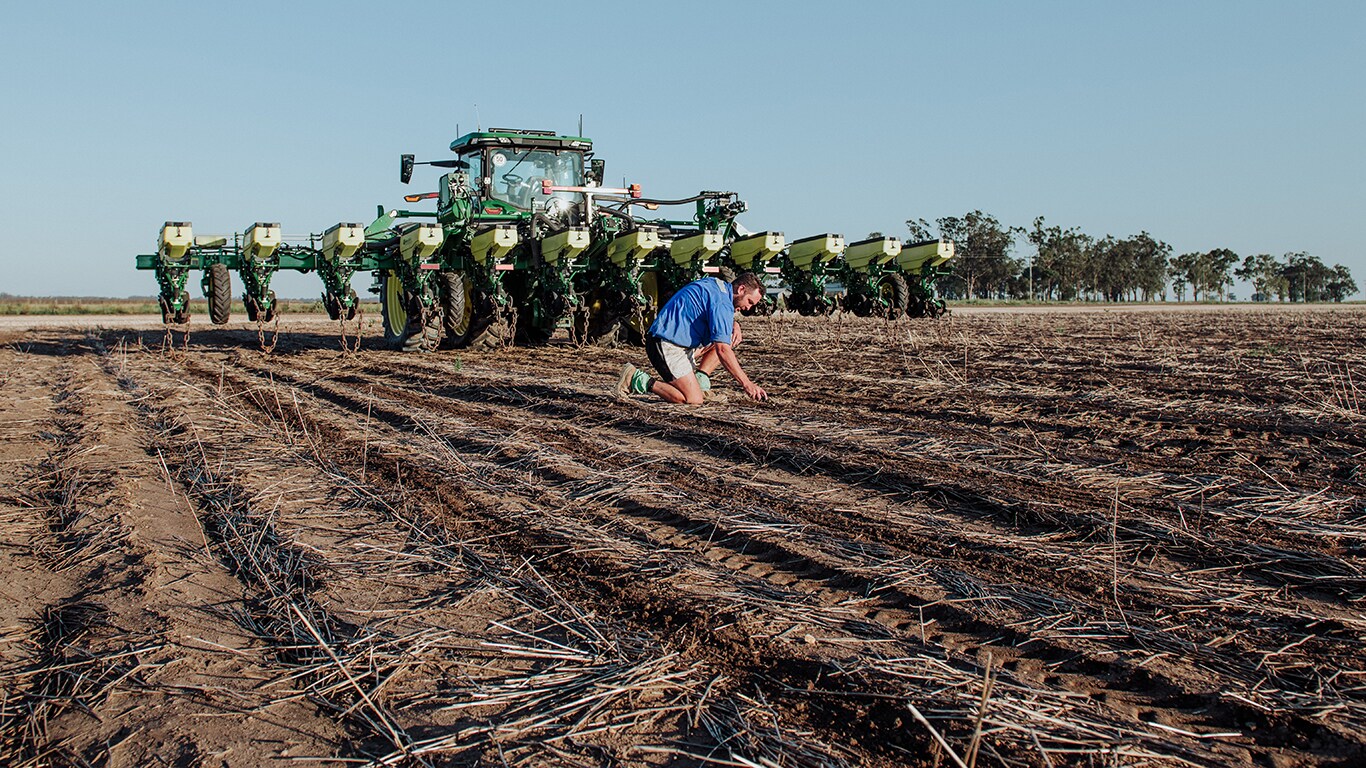 Farmer kneeling behind a John Deere tractor and planter