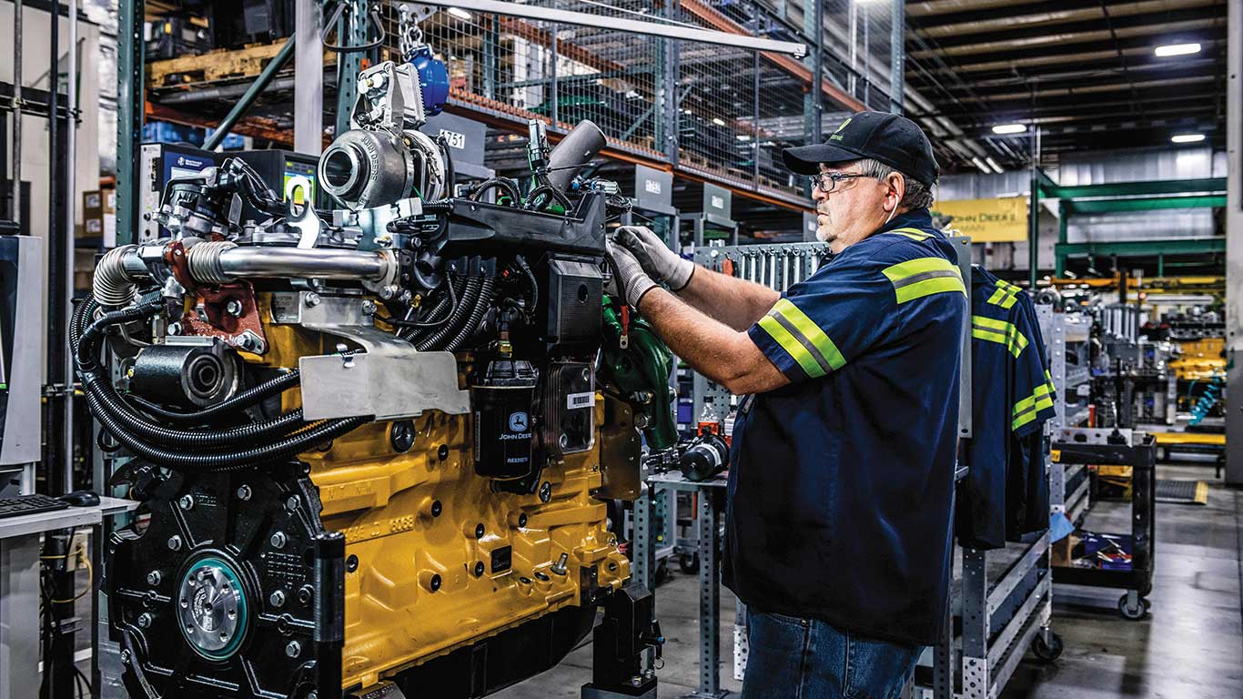 A John Deere factory employee is standing at his workstation in the Reman factory, fitting the final parts to an engine.