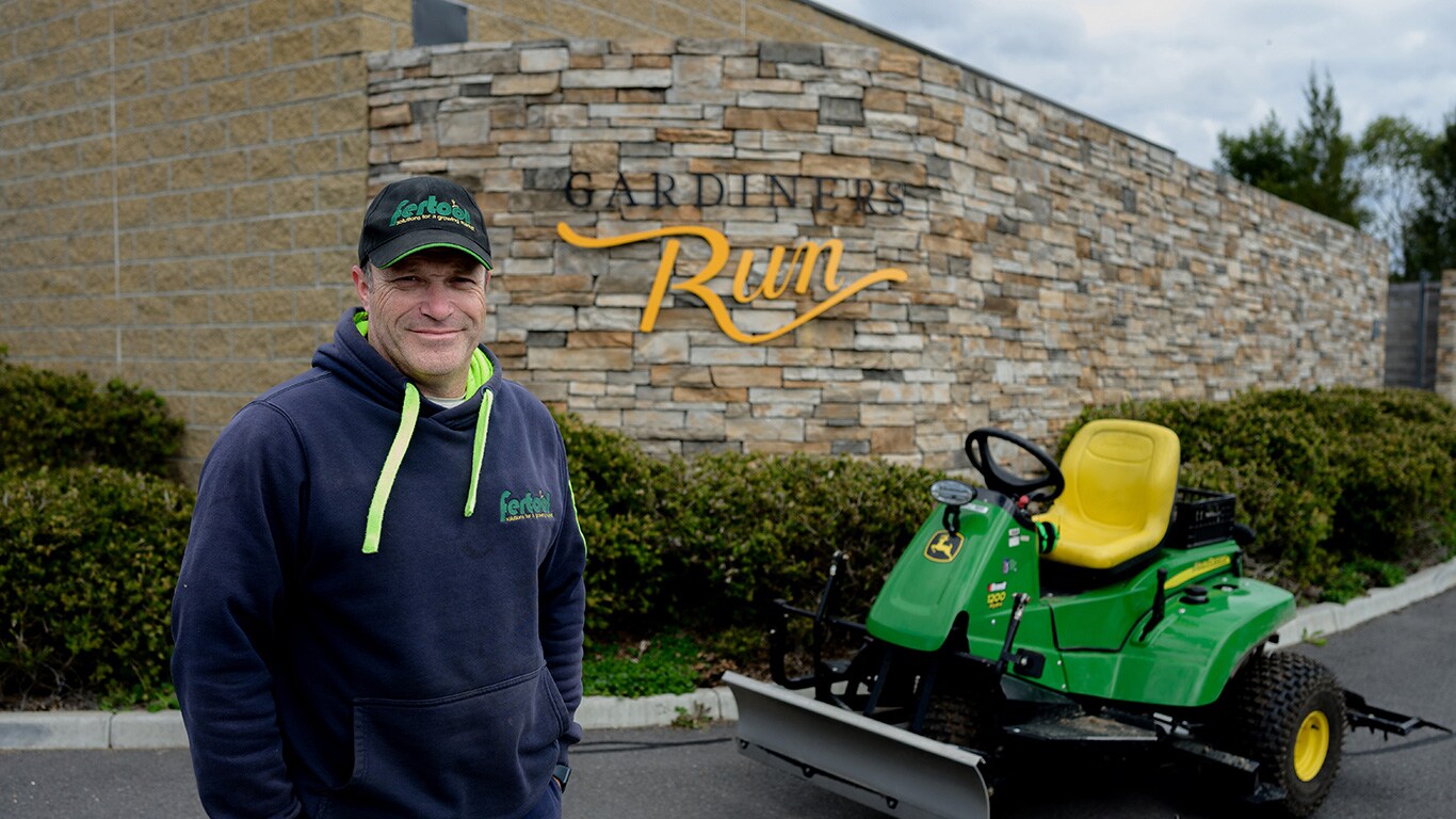 person standing next to John Deere equipment in front of a stone wall with the words "Gardiners Run"