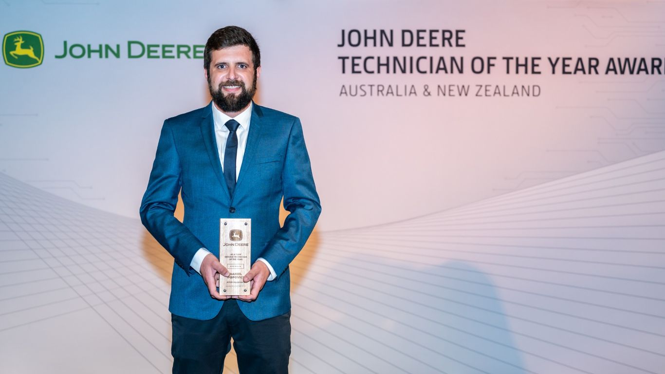 A man standing in front of a media wall holding a wooden trophy.