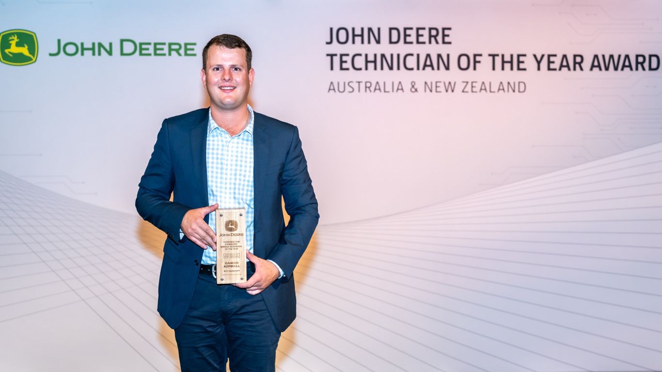 A man standing in front of a media wall holding a wooden trophy.
