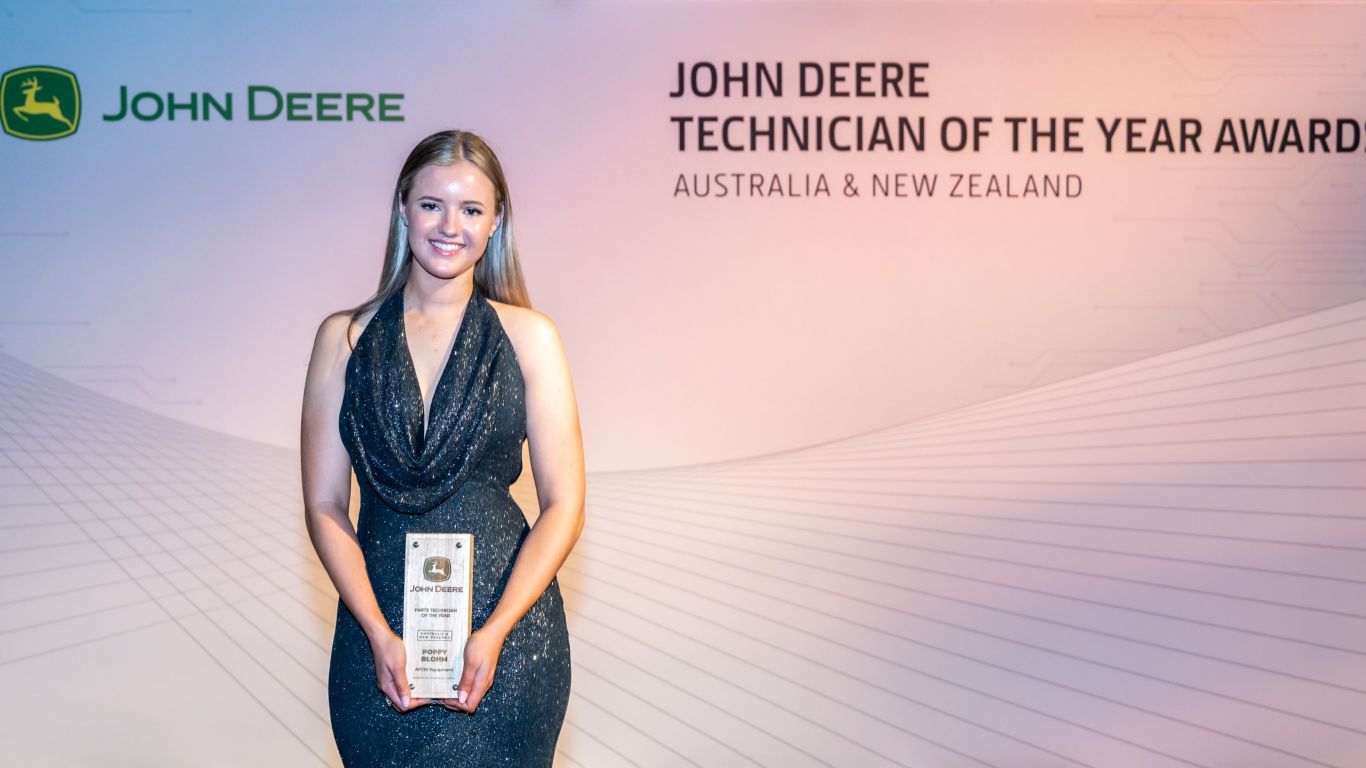 A lady standing in front of a media wall holding a wooden trophy.