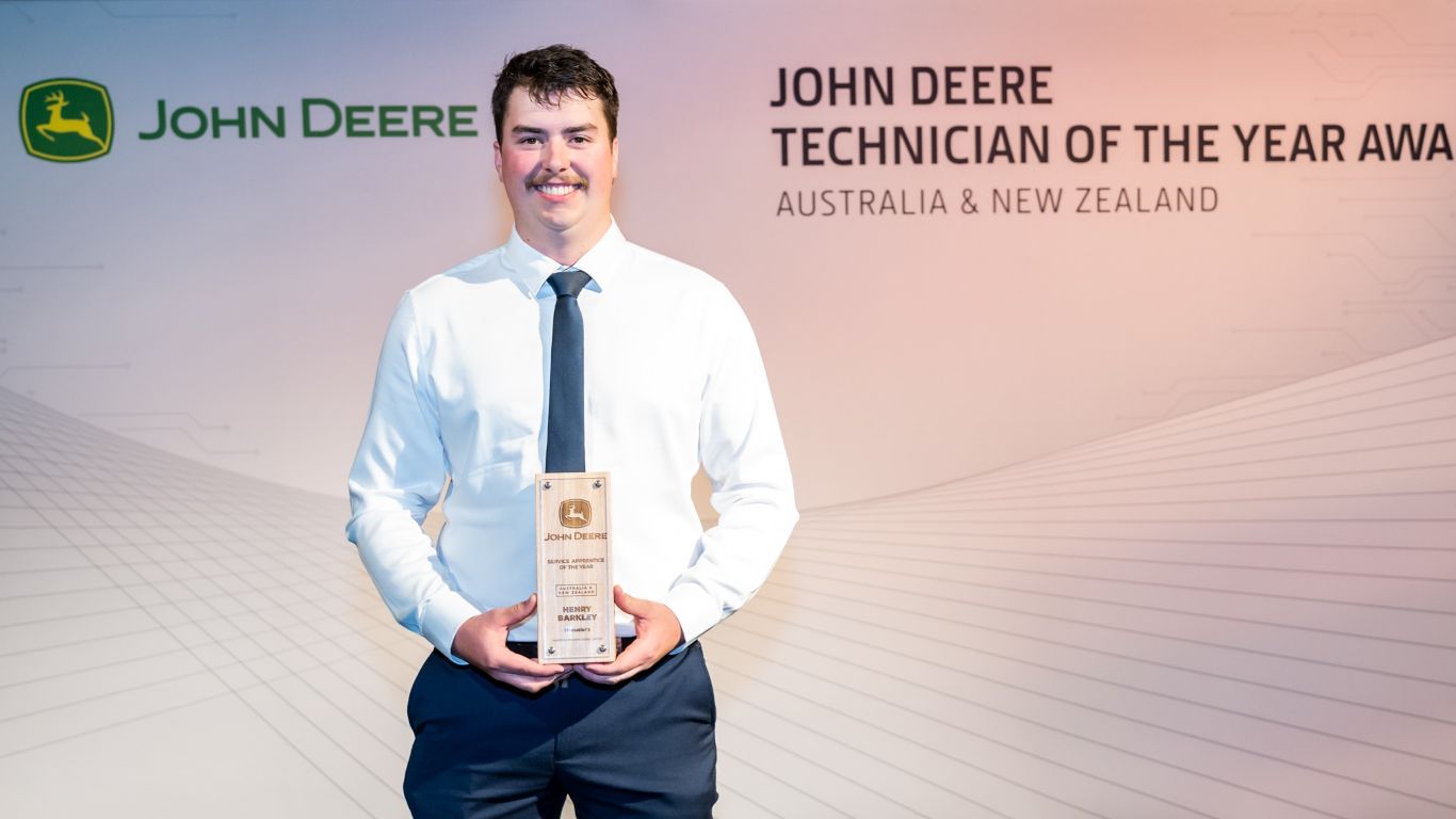 A man standing in front of a media wall holding a wooden trophy.