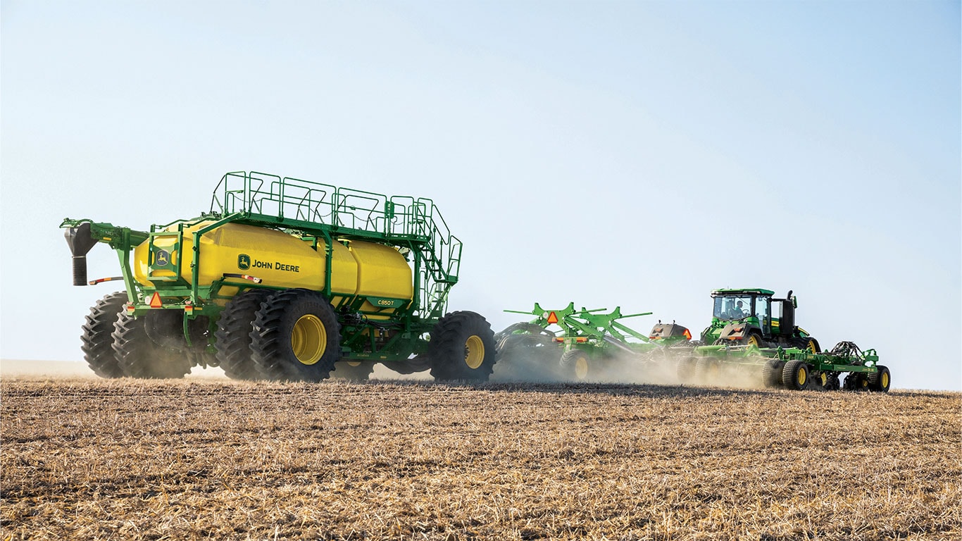 Close up of John Deere 9RX Tractor with P600 Precision Air Hoe Drill and C-Series Air Cart attached in paddock.