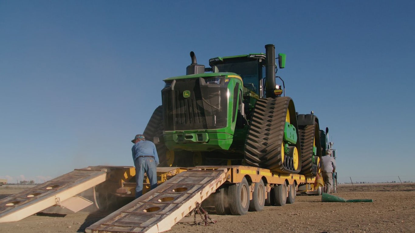 Large green 9RX tractor on truck trailer with man in blue shirt
