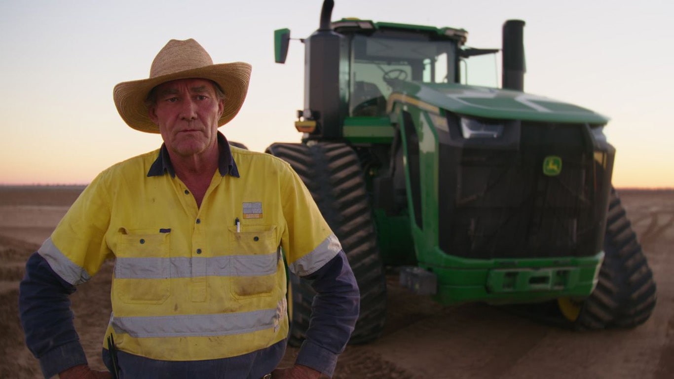 Man in yellow shirt and hat in front of large green tractor