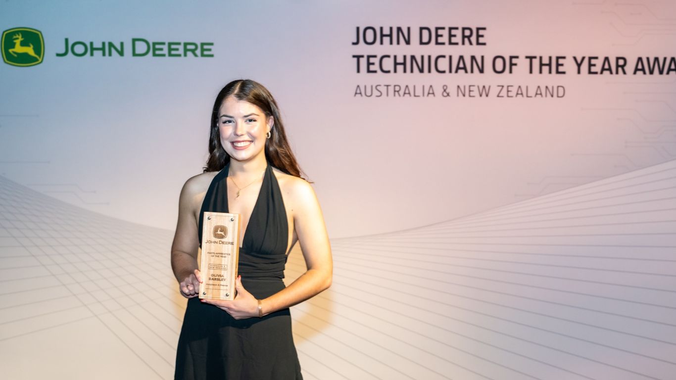 A lady standing in front of a media wall holding a wooden trophy.
