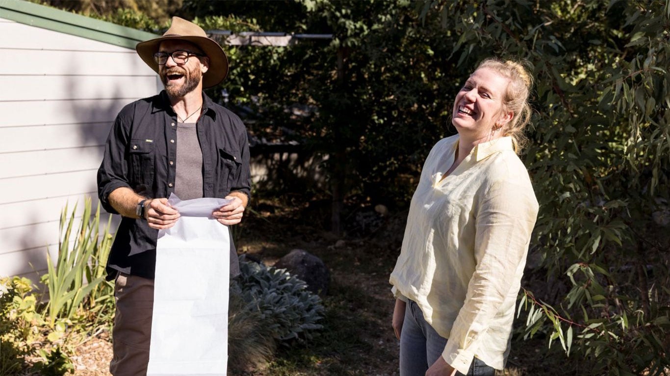 A man is holding a piece of long paper with a list of jobs and is laughing with a woman beside him who is also laughing.