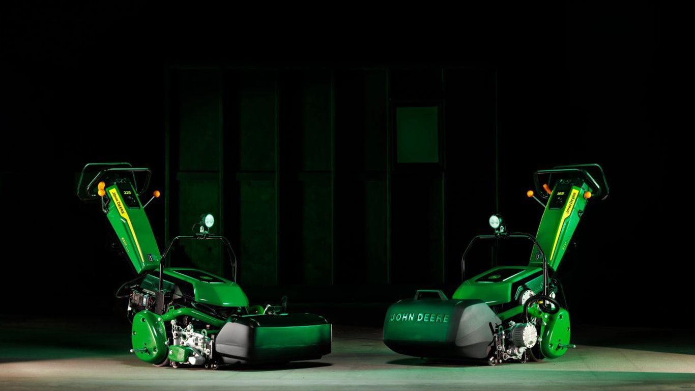 Two green professional walk behind mowers in a dark room.