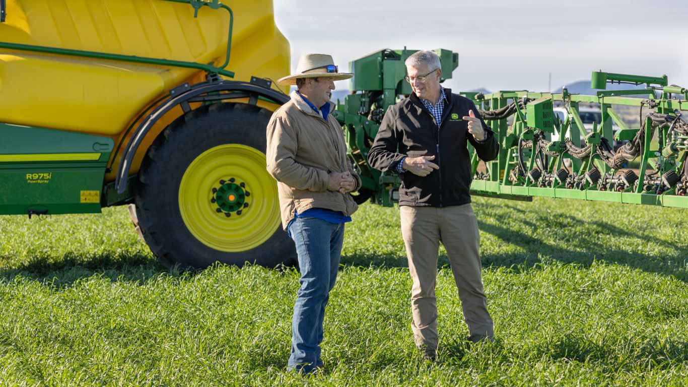Two men standing in paddock with spraying set up in the background