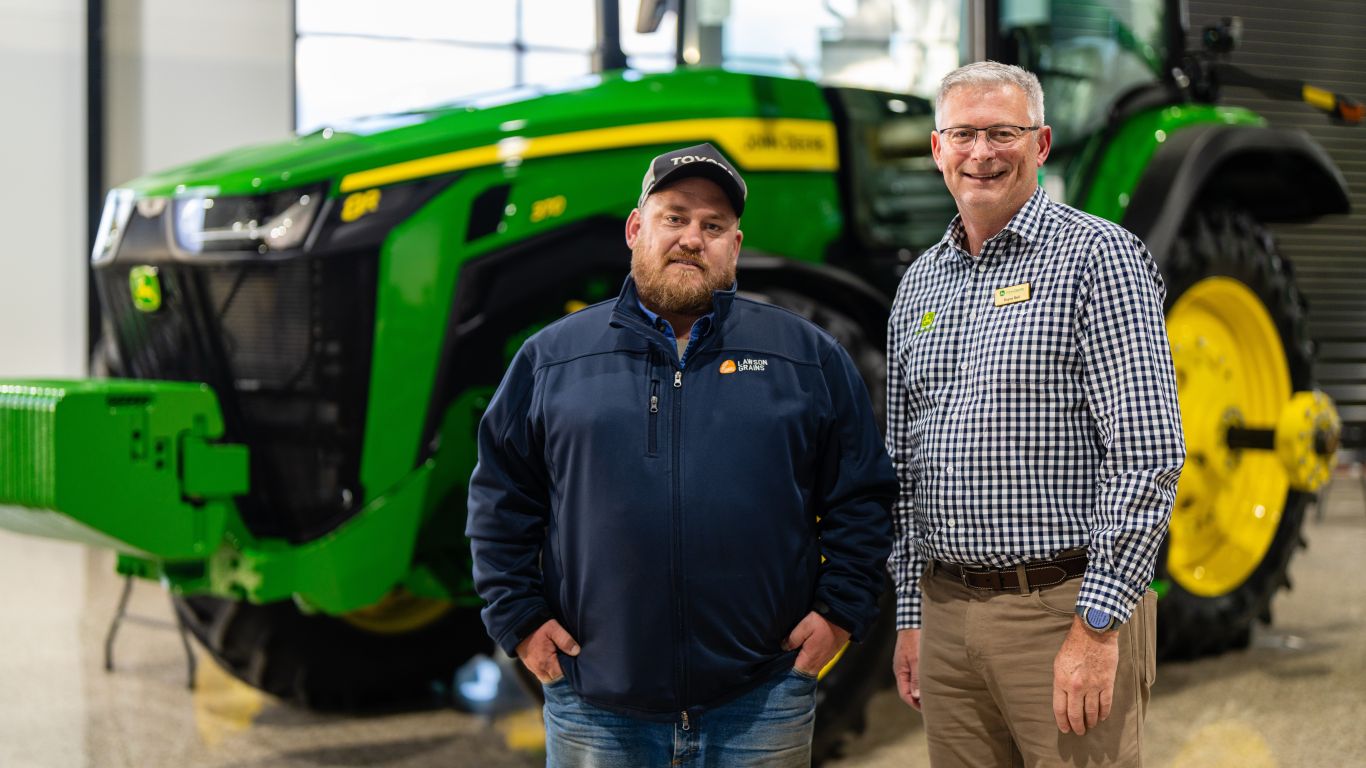Man navy jacket and man check shirt standing in front of green tractor inside