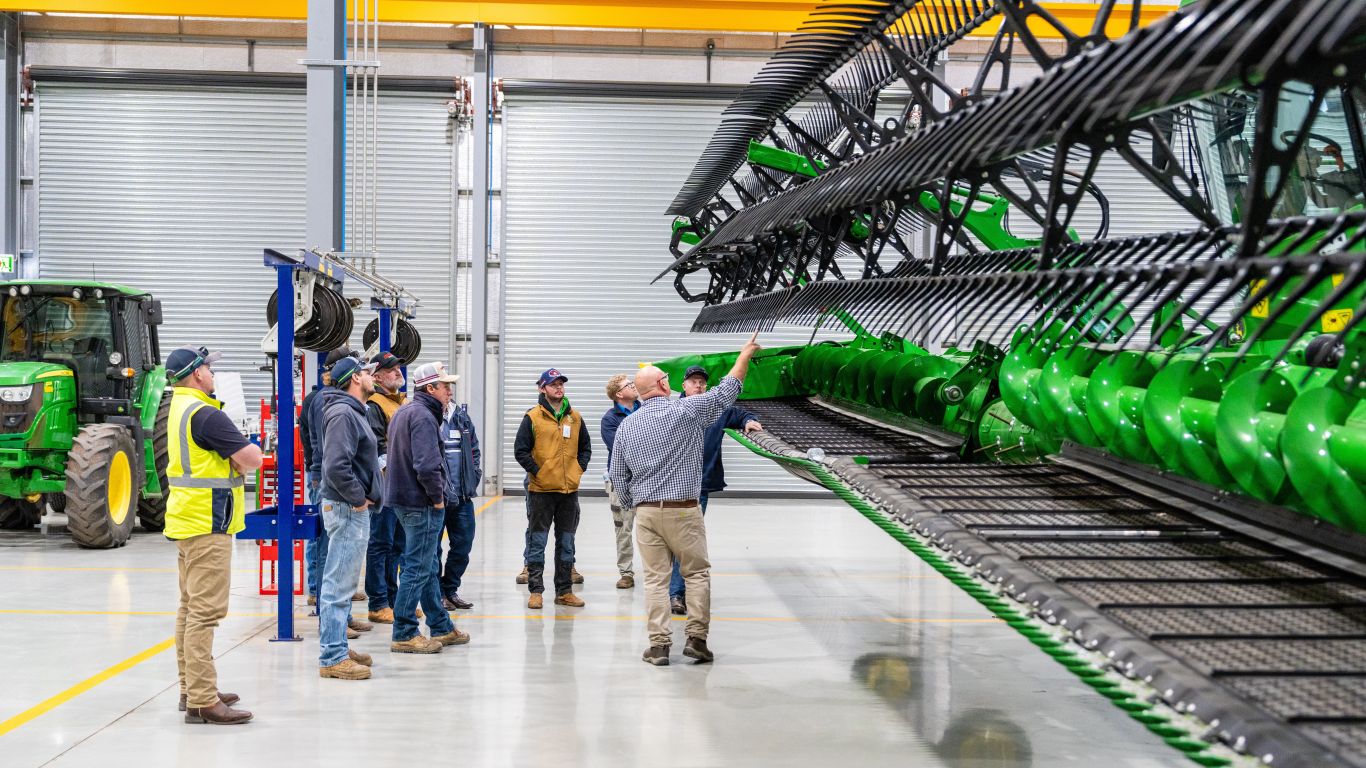Group of men looking at a green combine harvester in workshop