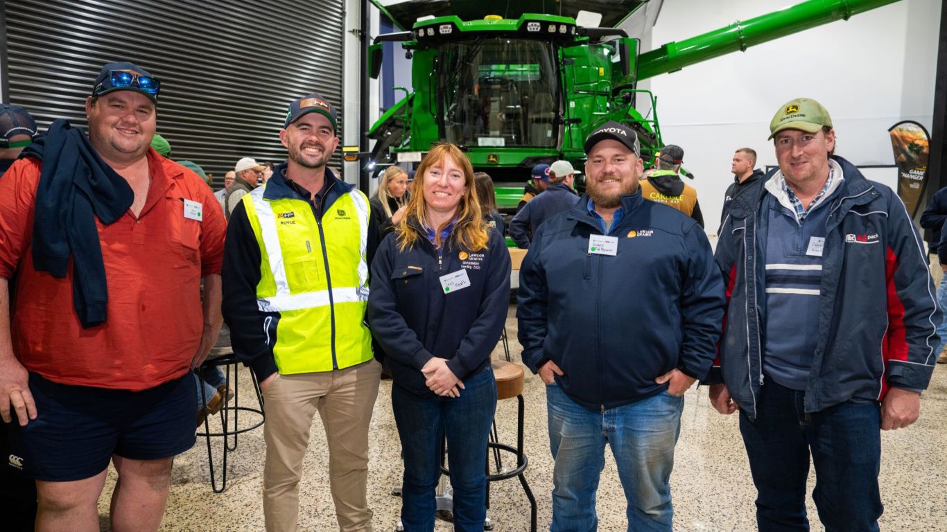 Group of people posed smiling in front of green combine harvester