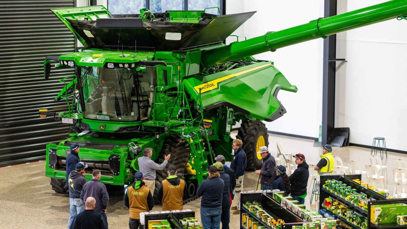 Group of people inside a dealership looking at a large green combine harvester