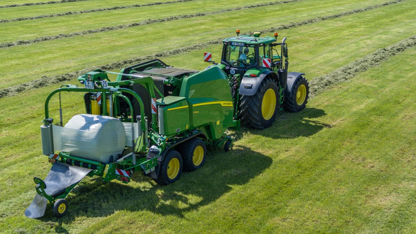 A John Deere tractor and baler in operation in a field.