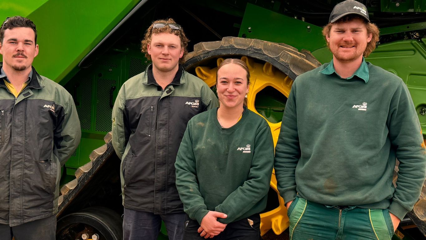 Three men and a women in green clothing standing in front of green machine.
